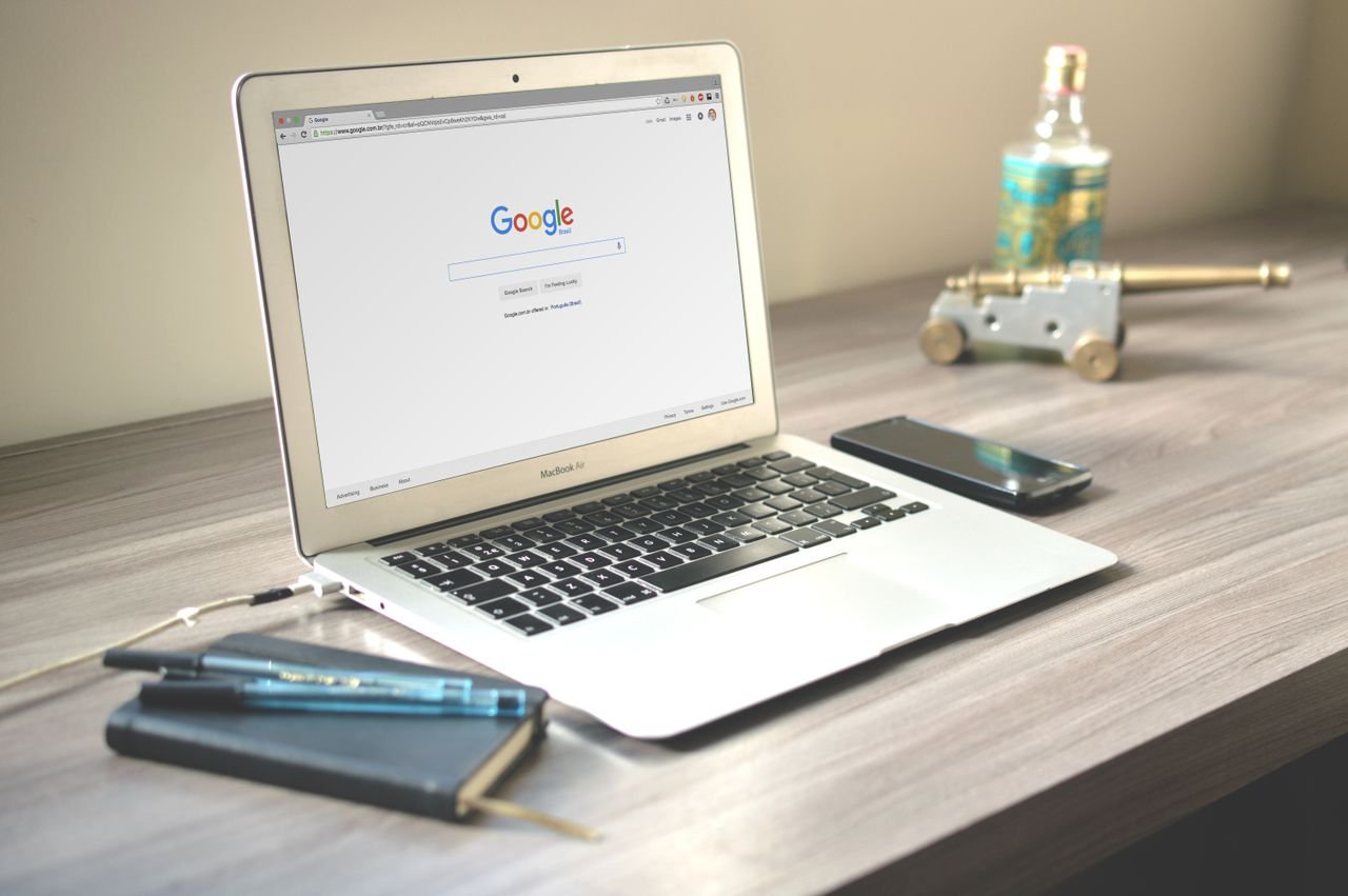 The Art of Drawing Readers In: Your attractive post title goes here A neat workspace featuring a laptop displaying Google search, a smartphone, and a notebook on a wooden desk.